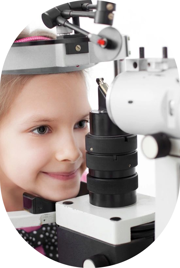 A young girl is looking through an eye exam machine.